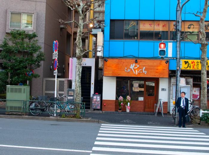 The exterior of a restaurant, featuring a bright blue facade, located across from a crosswalk.