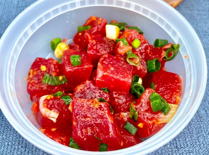 A plastic container filled with ahi poke adorned with toppings.