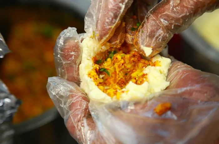 Gloved hands fill an aloo tikki patty.