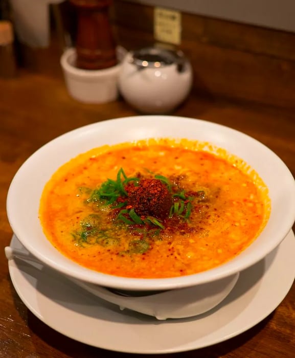 A vibrant orange bowl of broth, adorned with crumbled spice powder and seaweed.