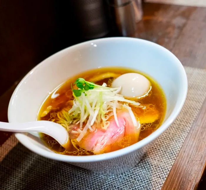 A towering bowl of ramen adorned with a mound of bean sprouts, bright pink slices of pork, and a soft-boiled egg floating in the savory broth.