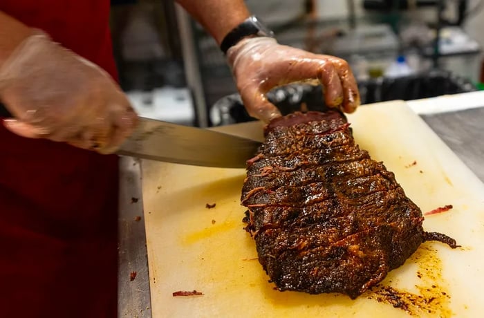 A chef carves brisket on a wooden board.