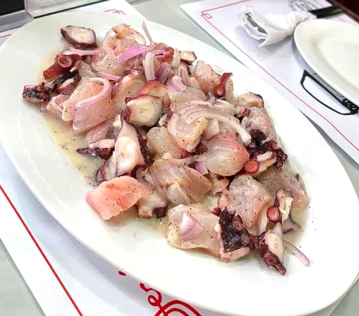 A lengthy plate of cebiche featuring octopus and onion.