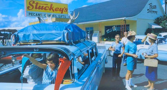 A 1970s advertisement for Stuckey’s truck stop chain depicts people chatting in the parking lot, with a little girl peeking out from the back of a blue station wagon packed for a road trip.