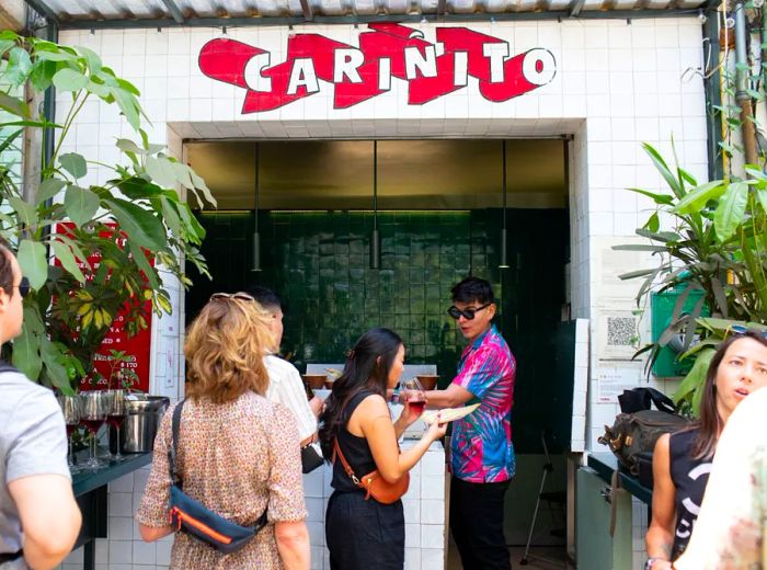 A small taco shop featuring an open kitchen, where customers line up as a cook in a floral shirt and sunglasses serves up delicious food.