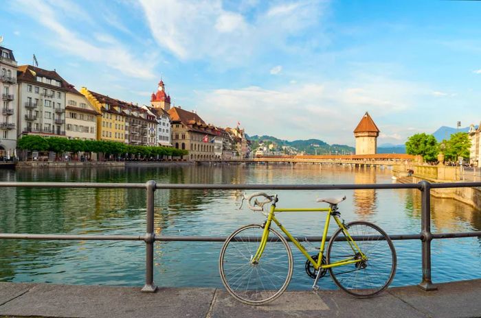 Cycle through the historic heart of Lucerne, featuring the iconic Chapel Bridge, all under a blue sky adorned with clouds.