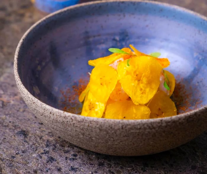 A mound of cebiche sits in a deep ceramic dish, surrounded by crunchy plantain chips, with a saucer of sauce on the side.