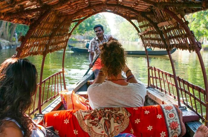 Two women enjoy a ride in a low-lying wooden boat, steered by a man.