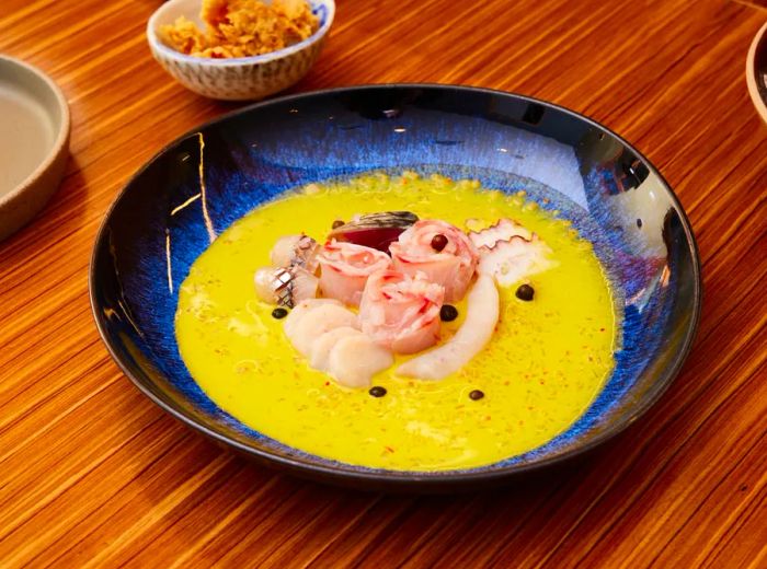 Elegant swirls of fish slices in a creamy yellow sauce, presented in a deep blue bowl on a wooden surface.