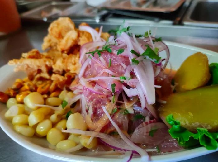 A dish of sliced fish heaped atop corn nuts, chicharron de calamar, and sweet potato.