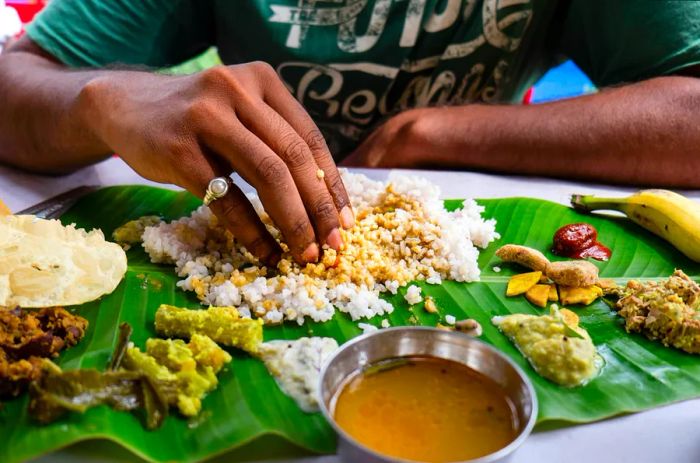 A man enjoys a banana leaf thali (plate meal) using his fingers in India.