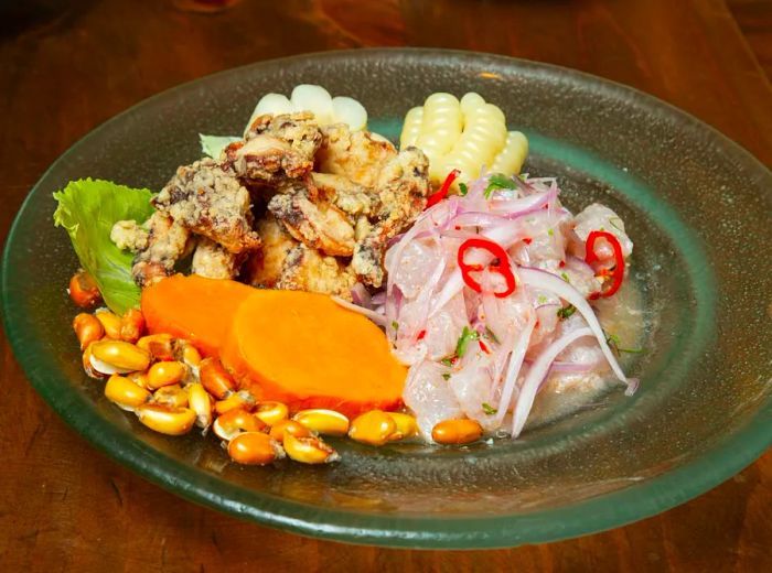 A dish of sliced fish served with sweet potato, crispy fried octopus, corn, corn nuts, and various accompaniments.