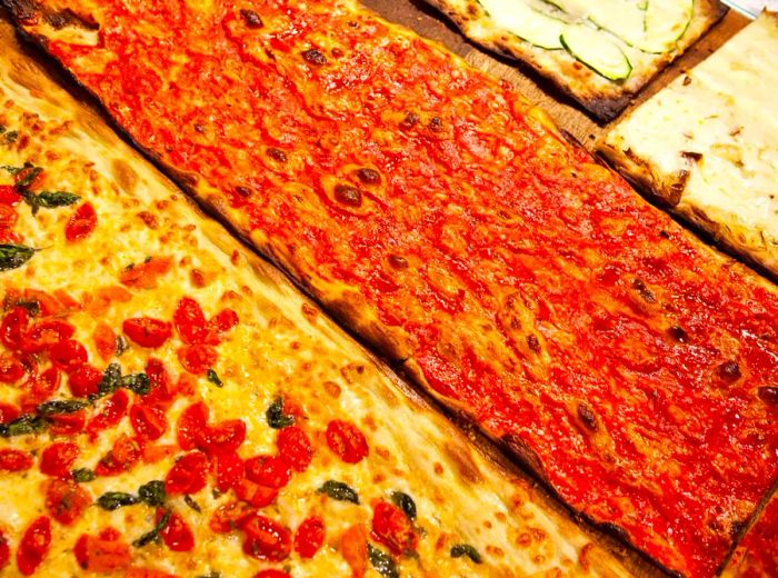 Long rectangular pizzas left uncut, showcasing one drenched in red sauce and another adorned with cherry tomatoes.