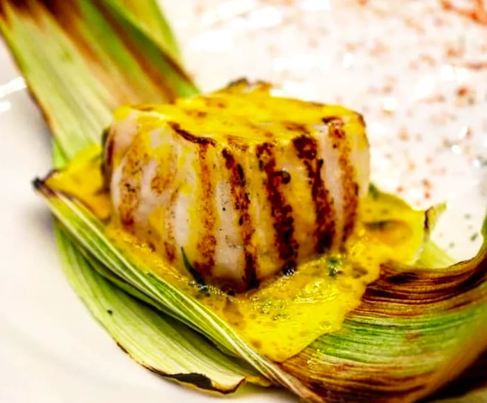 A block of grilled fish elegantly arranged in a sauce on a corn husk.