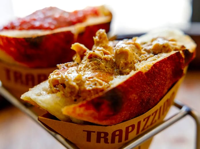 Two triangular trapizzino, one filled with saucy chicken and the other with a rich tomato sauce, displayed in a metal stand.