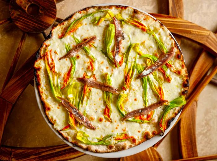 Aerial view of a white pizza topped with long strands of zucchini flowers and anchovies.