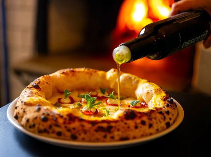 An individual pours olive oil onto a freshly made pizza featuring a thick crust.