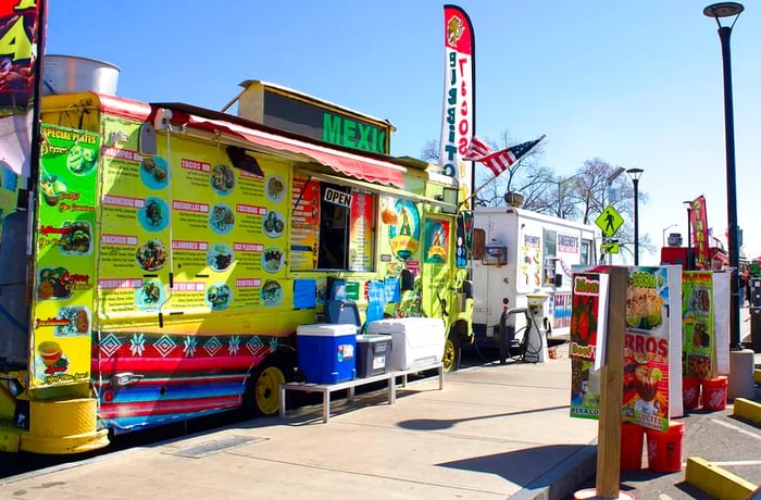 Food trucks lined up along a sidewalk, showcasing colorful menu boards and signs.