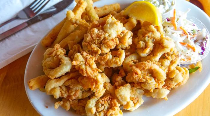 A serving of fried clams accompanied by fries, coleslaw, and a lemon wedge.