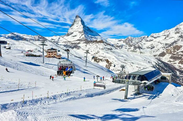 Skiers are boarding chair lifts at a lift station, with the Matterhorn looming in the background, in Zermatt, Switzerland.