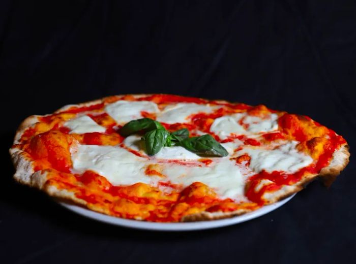 A thin margherita pizza displayed against a black background.