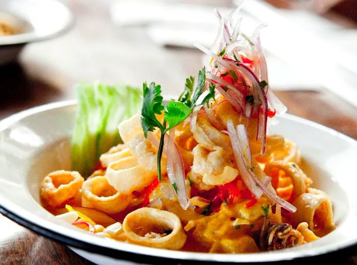 A generous serving of seafood dominates the plate, rising to a peak adorned with sliced onions and sprigs of cilantro.