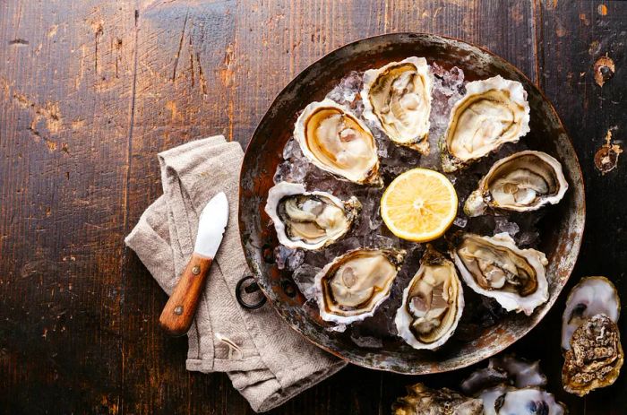 Opened oysters served on a copper plate against a dark wooden backdrop