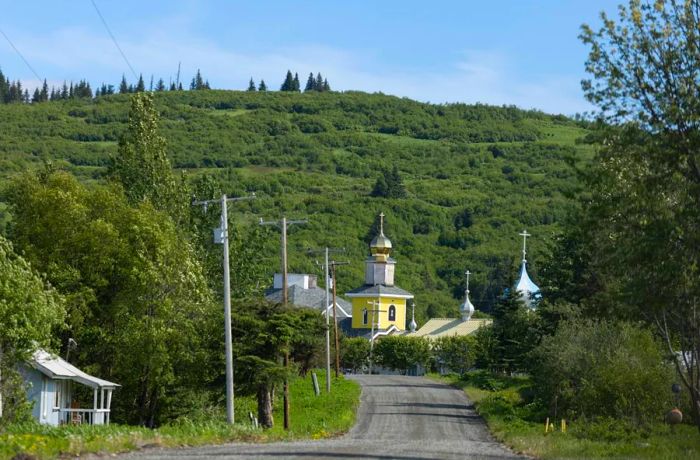 A vibrant yellow building topped with a golden dome stands out against the lush green hills and gravel road.