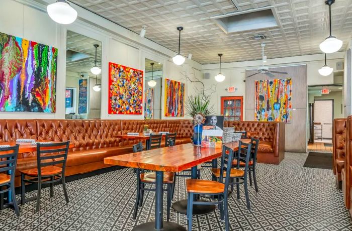 An interior view of a restaurant featuring textured tiled floors, vibrant canvases on the walls, and cozy leather banquettes.