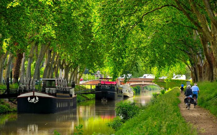 Barges navigate the Canal du Midi, while cyclists glide along the tree-lined towpaths in Toulouse, France.