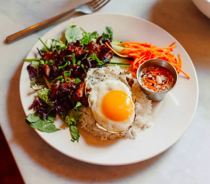 A dish featuring pork garnished with scallions and herbs, accompanied by a serving of rice topped with a fried egg.