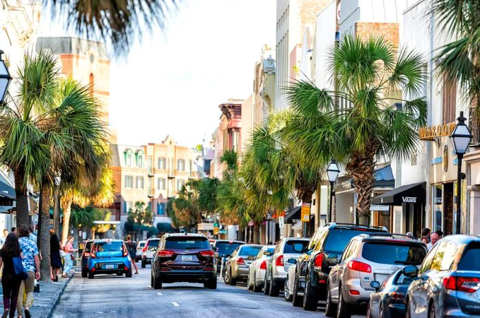 Downtown King Street in South Carolina bustling with people at sunset, lined with shops, restaurants, and parked cars.