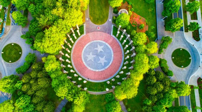 Aerial view of Bicentennial Capitol Mall showcasing trees and tall columns, with a circular stone at the center featuring the Tennessee flag emblem; weekend in Nashville.