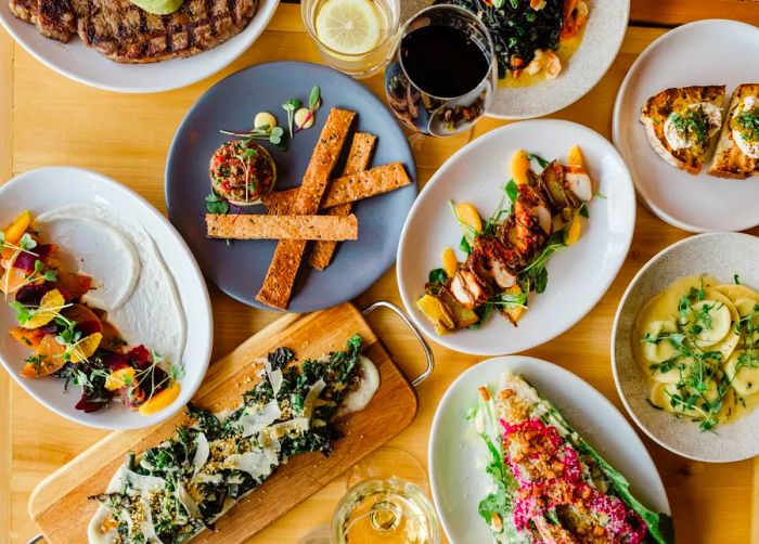 An assortment of dishes displayed on a rustic wooden table, featuring tartar, salad, egg-topped toast, and steak.