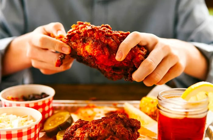 A person holds a sizzling chicken breast above a plate lined with red-checkered paper, accompanied by two side dishes in bowls. Nashville.