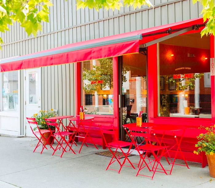 A vibrant red restaurant facade adorned with a red awning and matching metal tables and chairs.