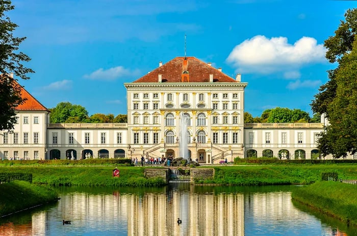 A picturesque view of Nymphenburg Palace (Schloss Nymphenburg), the former summer retreat of Bavaria's rulers, featuring swans in the reflecting pool, Munich, Germany.