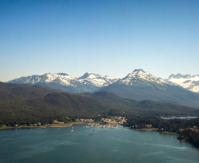 A picturesque view of snowy mountains and ocean with a quaint city along the coastline.