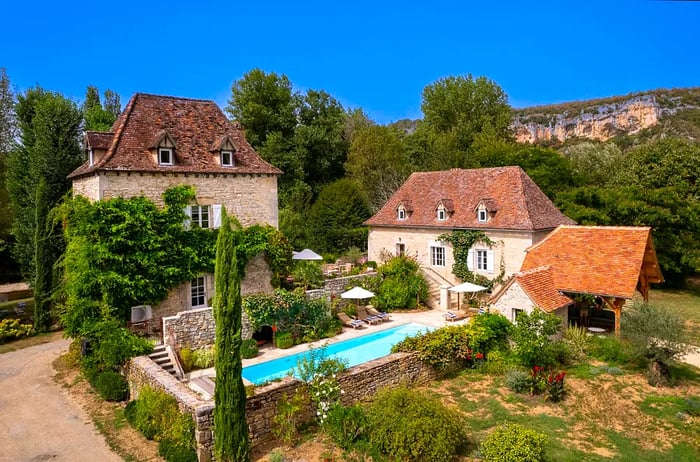 A sprawling countryside estate features a blue swimming pool enclosed by stone walls.