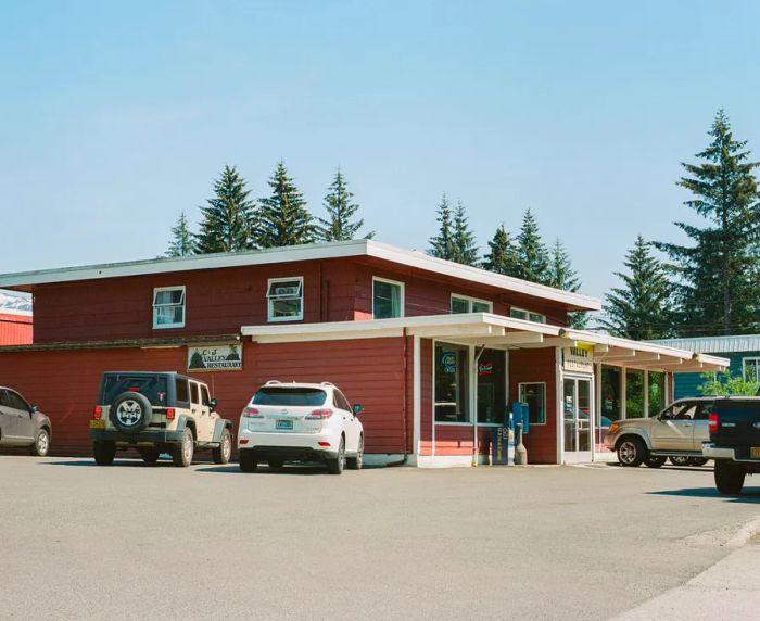 A vibrant red building with white trim, framed by green trees in the background, and cars parked out front.