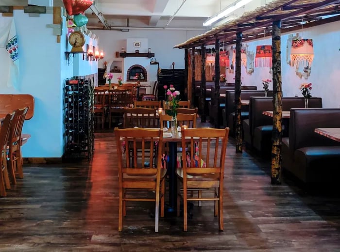 The dining area features wooden chairs and tables, lined with booths and accented by a fireplace at the back, with white walls and wooden floors.