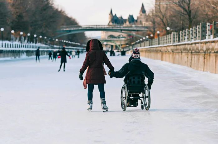 A couple enjoys the frozen canal, one on skates and the other in a wheelchair