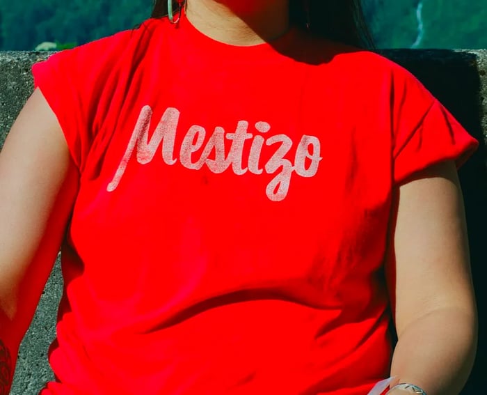 A close-up image of a girl in a red shirt emblazoned with the word 'Mestizo' in elegant white script.