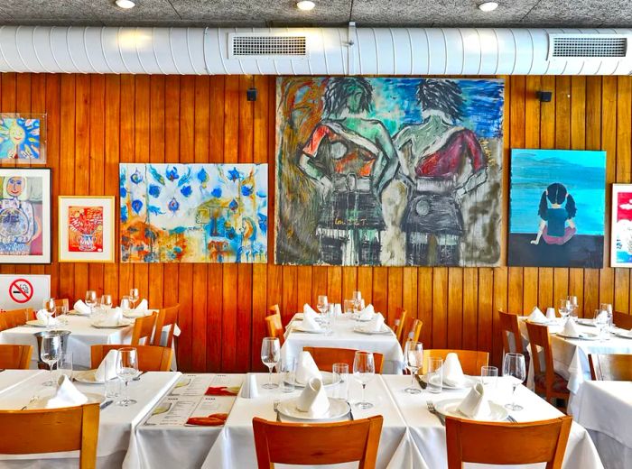 A cozy dining area featuring wood paneling adorned with vibrant illustrations and elegantly set tables draped in white tablecloths.