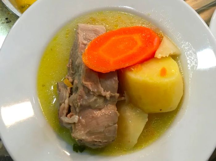 A top-down view of a generous serving of boiled meat, carrots, and potatoes in broth.