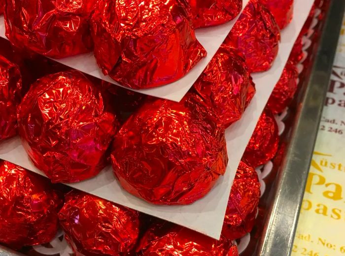 A collection of chocolates wrapped in red foil, neatly arranged on sheets of parchment paper.