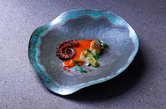 A large, shell-shaped plate showcasing octopus and vegetables nestled in a delicate sauce.