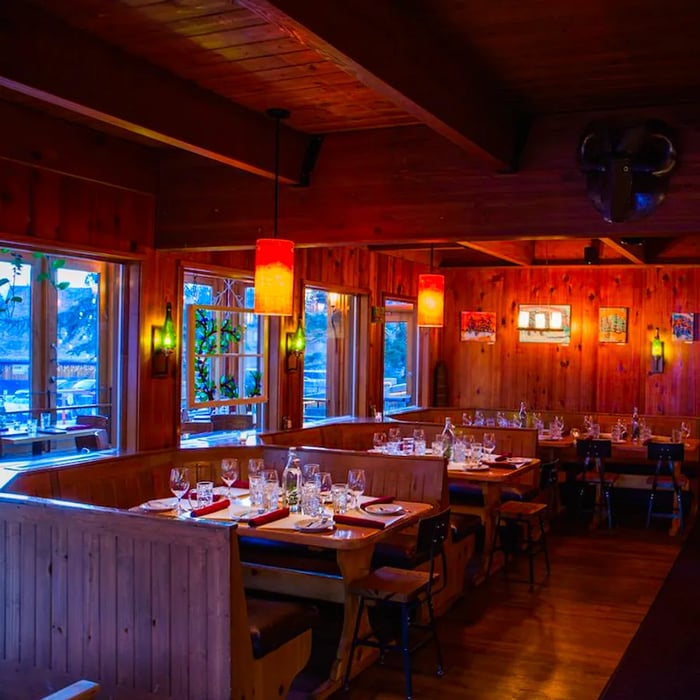 A dining area adorned with warm wood paneling and soft pendant lights illuminating booth tables set for an evening meal.