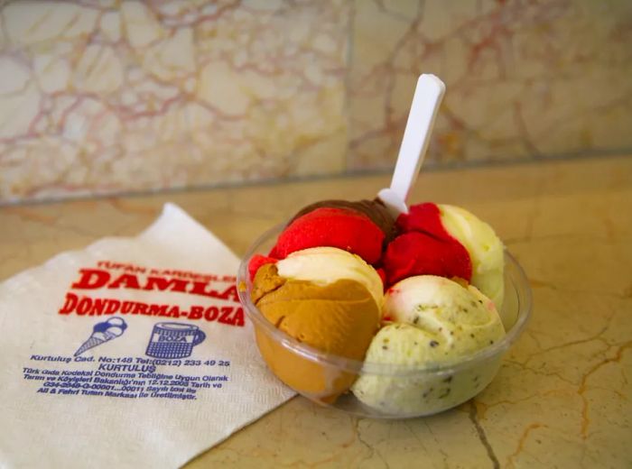 A clear plastic bowl filled with vibrant scoops of ice cream and a spoon, resting on a counter with a branded napkin.