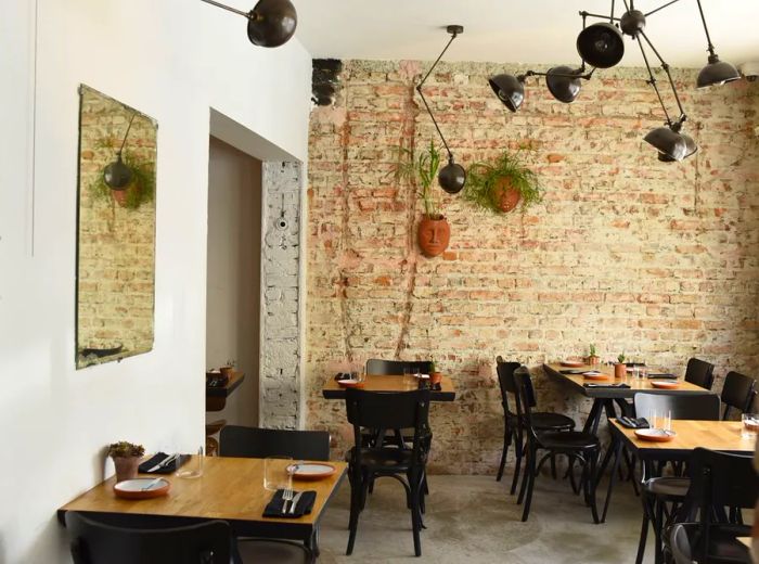 A dining area featuring an exposed brick wall adorned with whimsical octopus-shaped pendant lights, complemented by empty wooden tables prepared for dining.